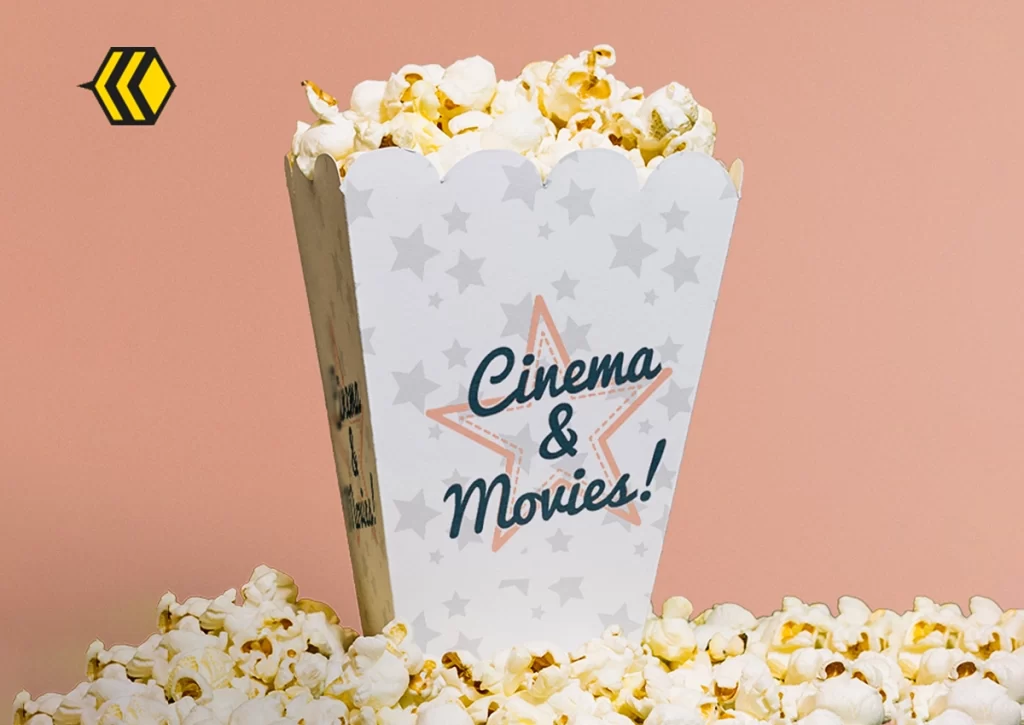 A white popcorn box labeled Cinema & Movies! is filled with popcorn and surrounded by more popcorn